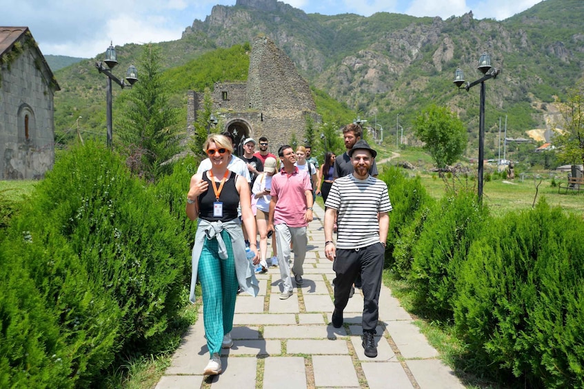En grupp människor promenerar på en stenlagd stig, omgiven av grönska och historiska byggnader i sten. 5