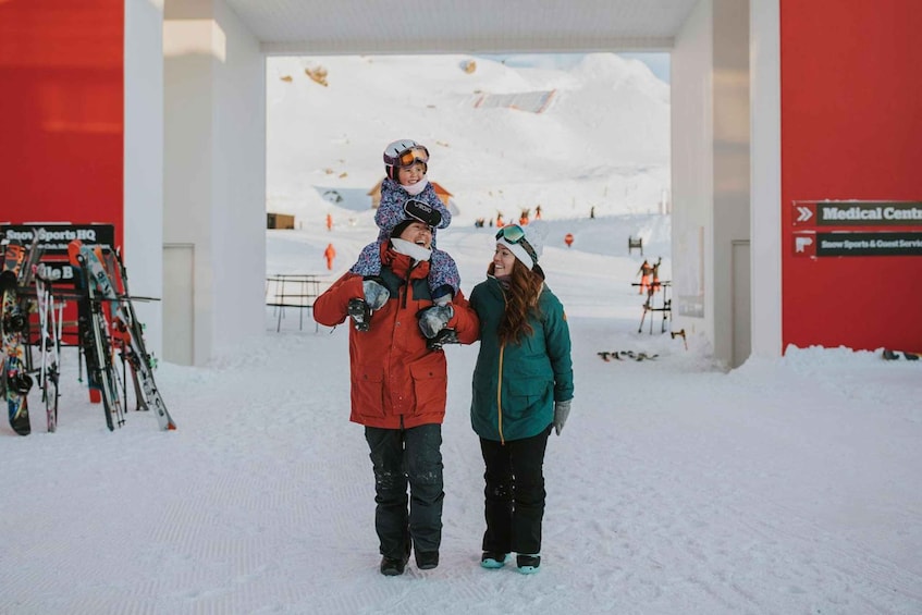 A snowy ski resort with a medical center sign, ski equipment, and a person carrying a child on their shoulders. 2