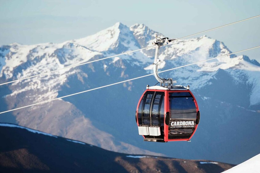 A cable car with 'CARDRONA' written on it, suspended above a snowy mountain range. 1