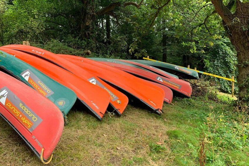 A row of red and green canoes lined up on grass with trees in the background. 5