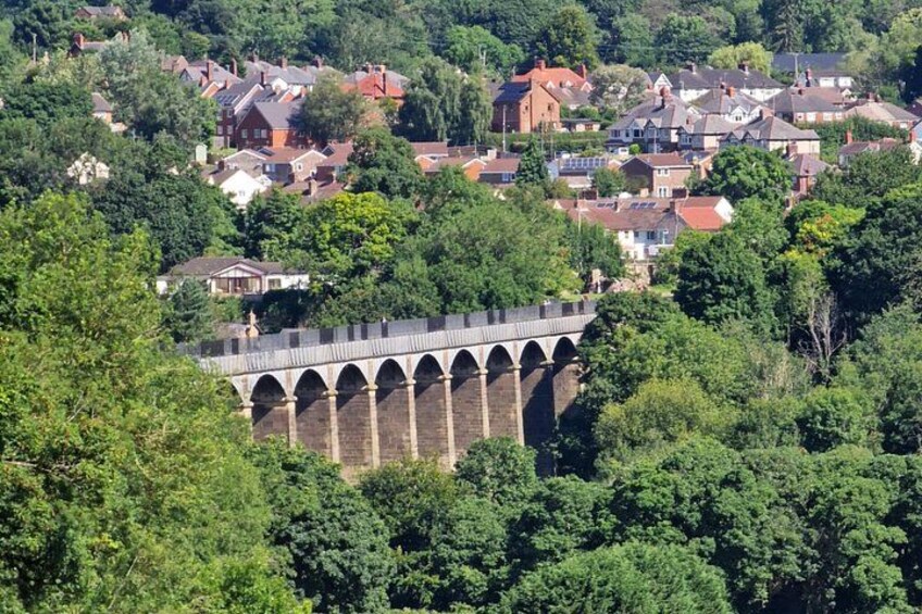 A stone bridge with arches, surrounded by lush greenery and residential houses. 3