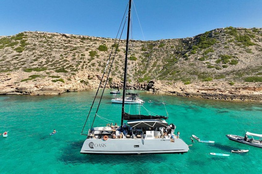 Un velero llamado 'Oasis' fondeado en aguas turquesas, con una costa rocosa al fondo. 1