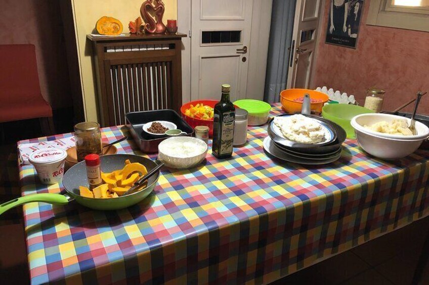 Une table sur laquelle on trouve divers aliments et condiments, notamment des bols de purée de pommes de terre, un saladier de fruits et une bouteille d’huile d’olive. 2