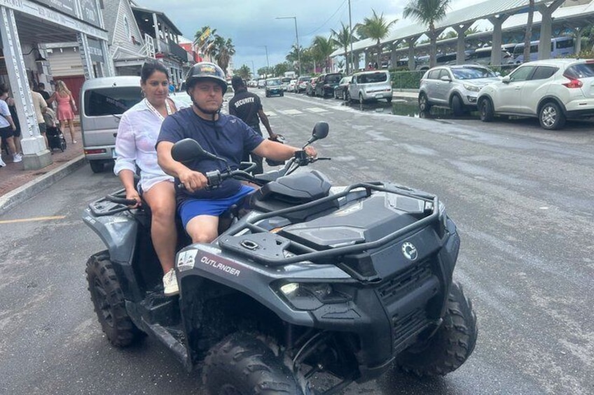 A person riding an ATV on a street with parked cars and buildings in the background. 4