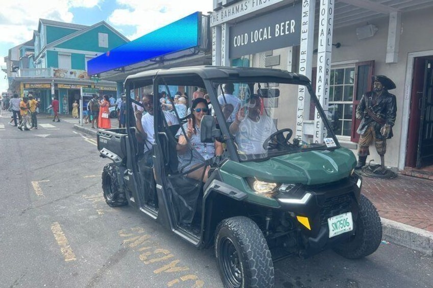 A green jeepney with passengers, parked in front of a building with a sign reading 'COLD LOCAL BEER.' 2