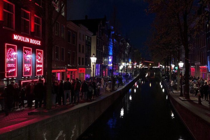 A canal with buildings on either side, including a brightly lit establishment with neon signs. 2