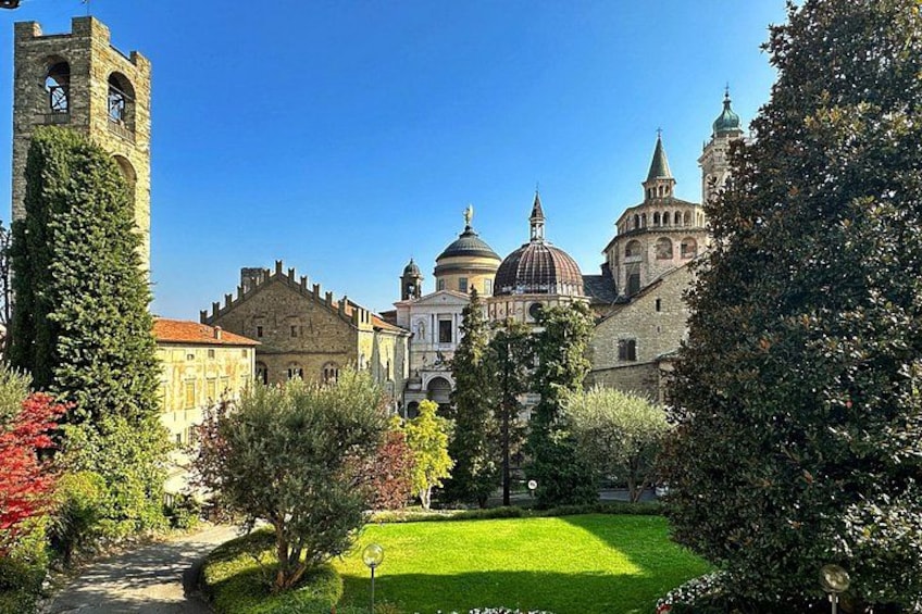 A historic building complex with a tower, domed structures, and a well-maintained garden. 2