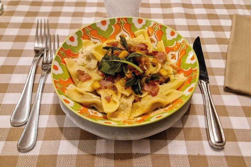 Ein Teller Pasta mit Gemüse und Speck auf einer karierten Tischdecke. 3