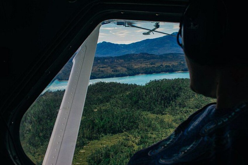 En helikopter flyger över ett skogsområde med en sjö och berg i bakgrunden. 5
