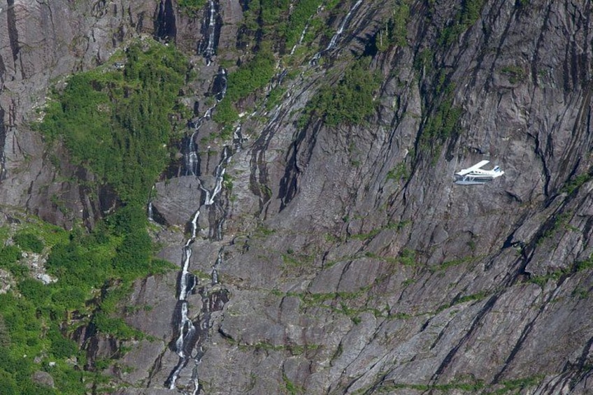 Ett vitt flygplan på en klippig klippa med ett vattenfall i bakgrunden. 4