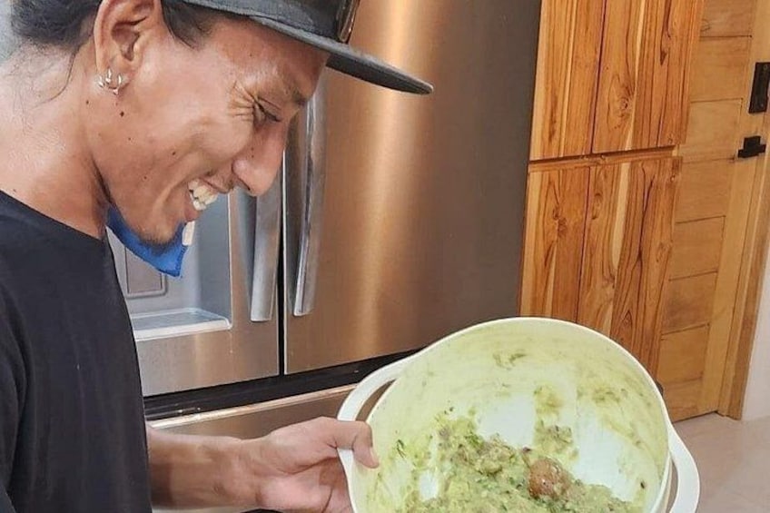 Une personne tenant un bol contenant une substance verte, debout dans une cuisine équipée d’un réfrigérateur en acier inoxydable et de meubles de rangement en bois. 4