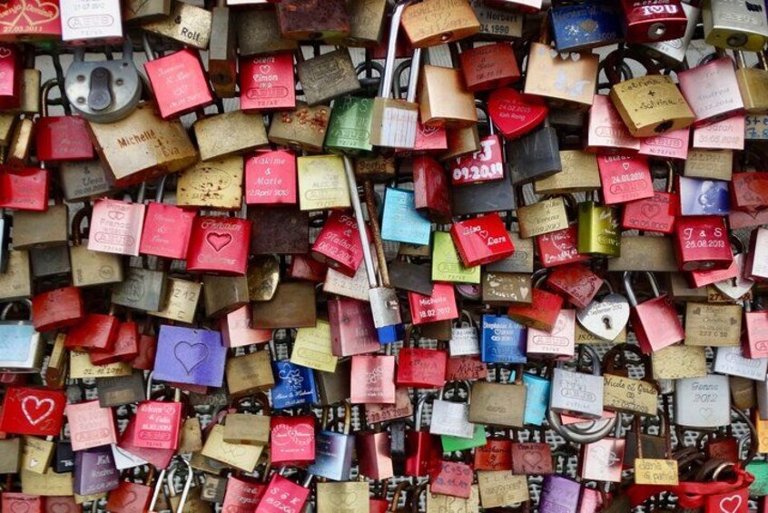 A wall covered with numerous padlocks, each with a name and date on it. 3