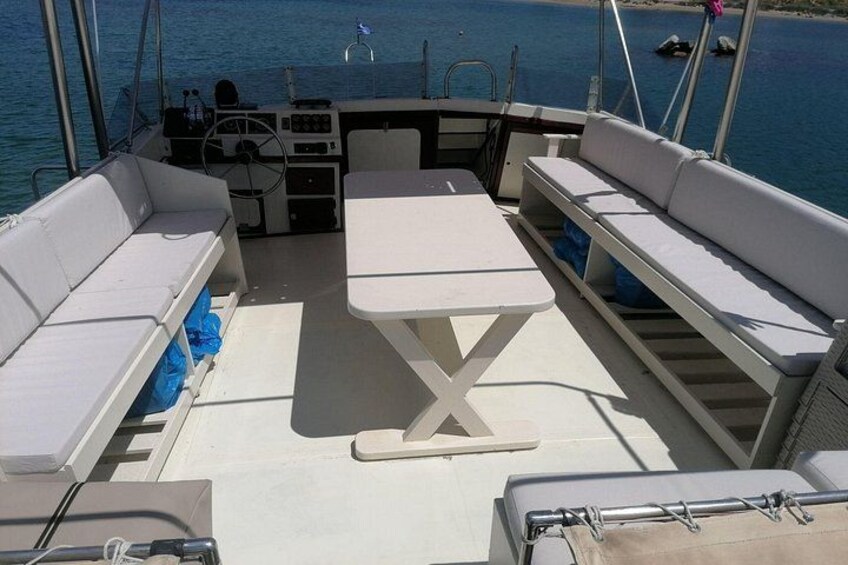A boat's deck with white cushioned seating, a central table, and a steering wheel. 4