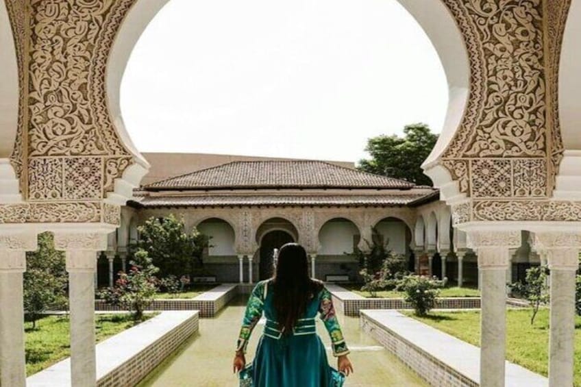 A woman in a green dress walking through an ornate courtyard with intricate arches and a tiled roof. 2