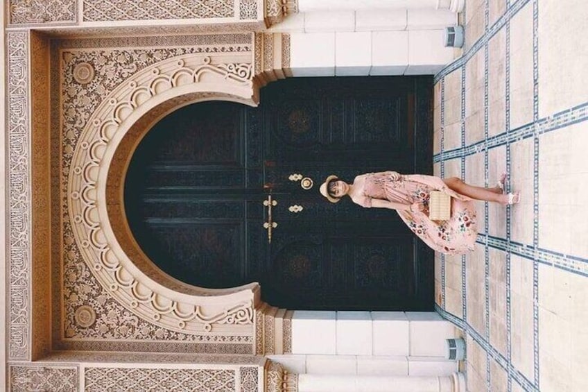 A woman standing in front of a large, ornate black door with intricate designs. 5