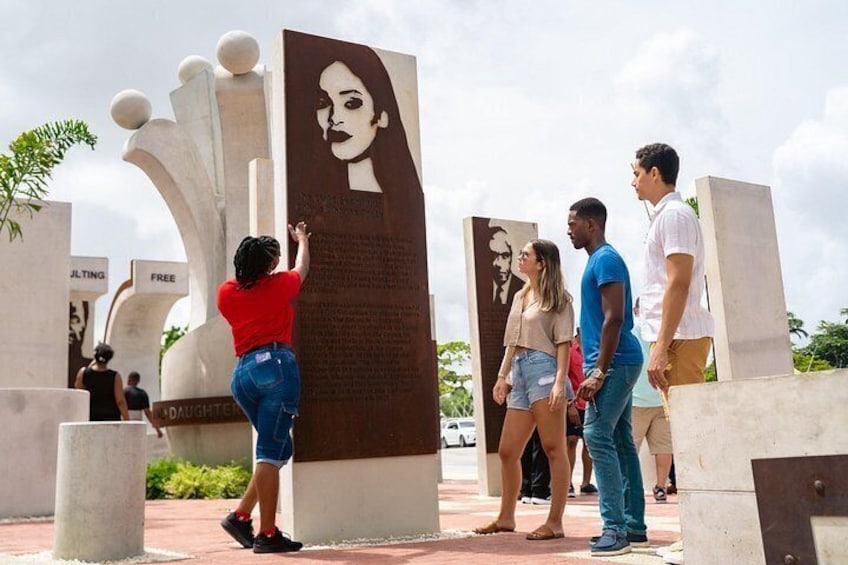 A group of people standing in front of a large monument with inscriptions and a portrait. 3