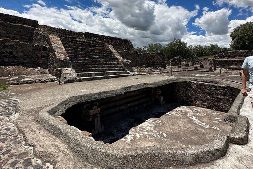 An ancient stone structure with a large central pit and steps leading up to a platform. 5