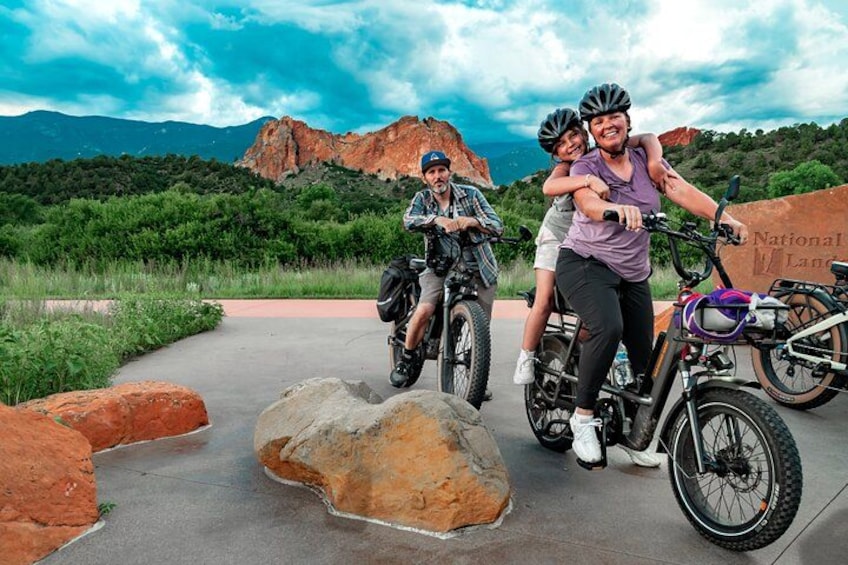 Three people on bicycles, a rocky path, and a mountainous landscape with a clear sky. 2