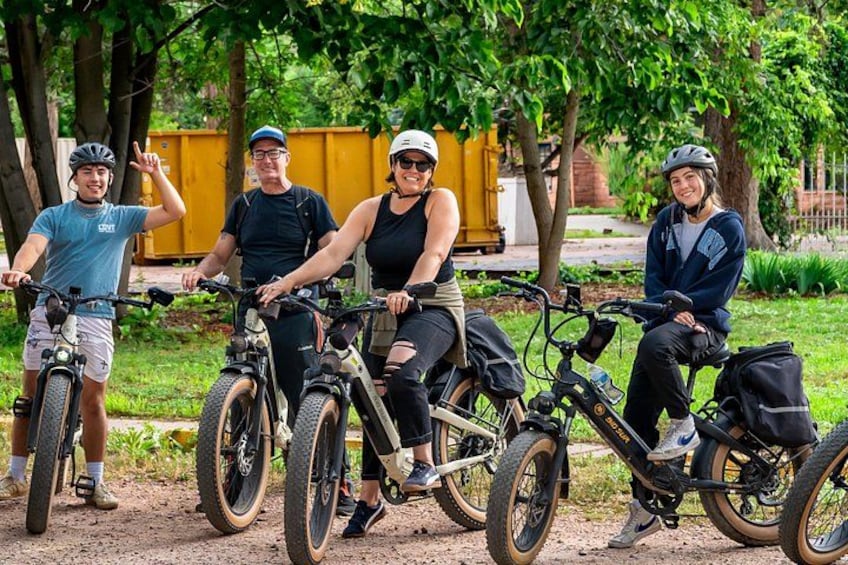 Four people on bicycles in a park with trees and a yellow dumpster in the background. 2
