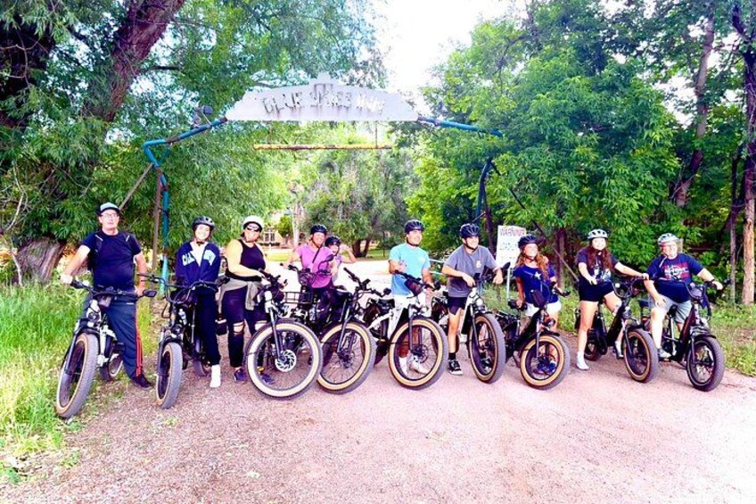 A group of cyclists posing for a photo in a forested area with a sign overhead. 4