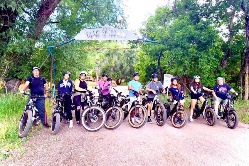 A group of cyclists on a dirt path with trees and a sign in the background. 4