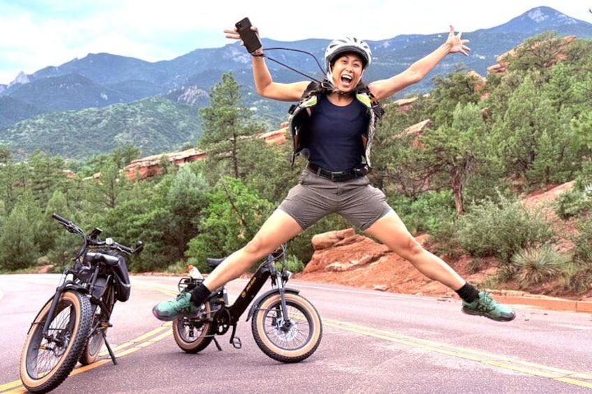 A person jumping in front of a mountain landscape with a bicycle. 1