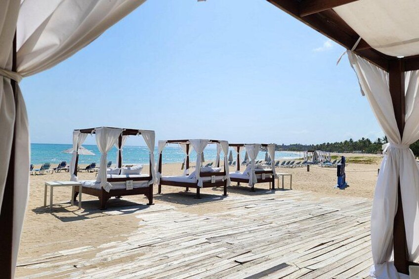 Une plage avec une terrasse en bois, des parasols blancs et des chaises longues. 4