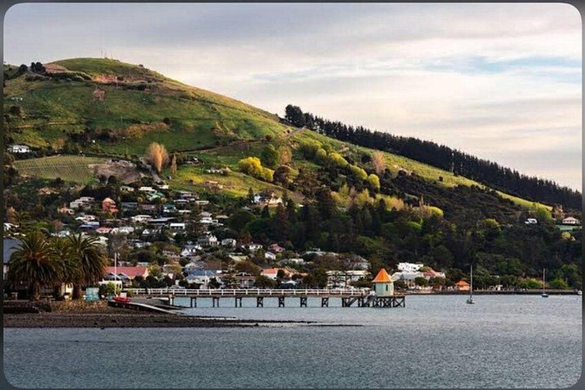 A coastal town with houses on a hillside, a pier extending into the water, and a clear sky. 5