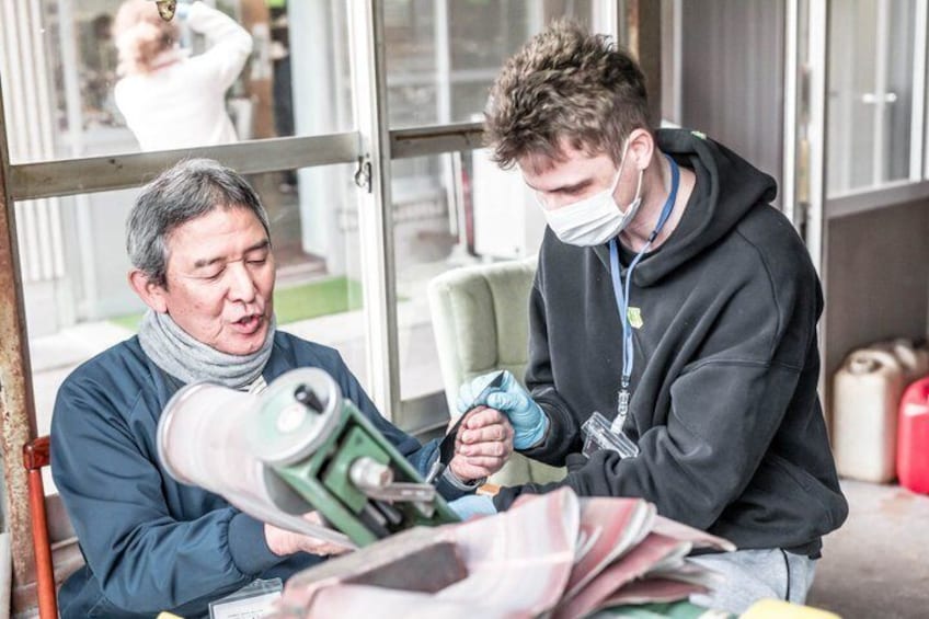 Two people examining a large green machine, possibly a press or press machine, in an industrial setting with metal structures and a glass door. 4