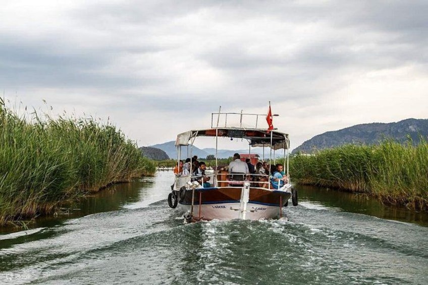 A boat with passengers on a river surrounded by tall grass and hills. 3