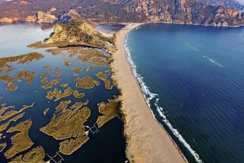 A coastal landscape with a sandy beach, rocky outcrops, and a clear blue sea. 2