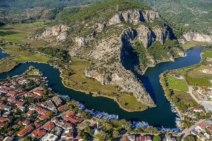 A river winding through a mountainous landscape with a town on one side and a rocky outcrop on the other. 5