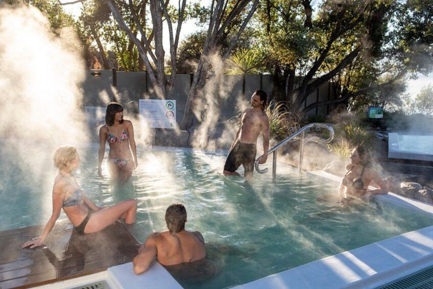 A pool with people swimming and sitting, surrounded by trees. 4