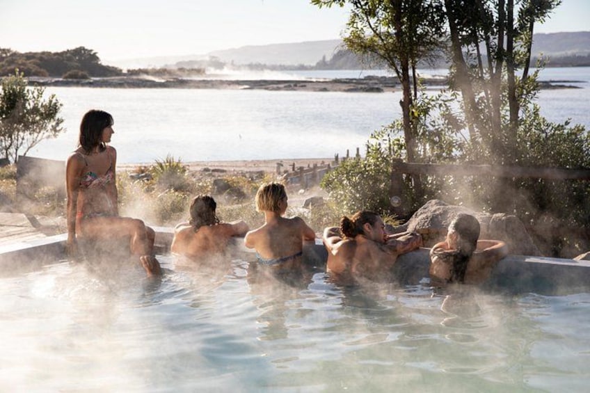 A group of people in a hot spring bath with a view of the sea and hills in the background. 5