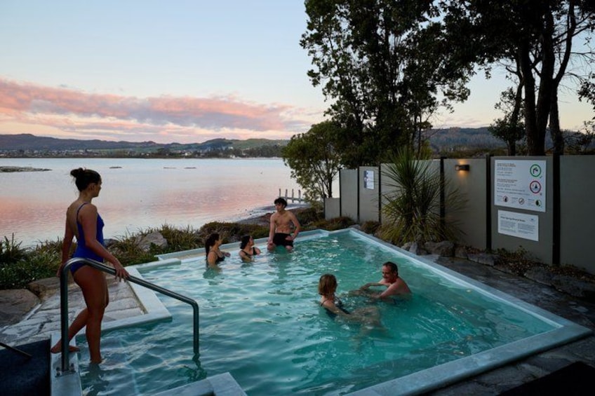 A swimming pool with people in it, surrounded by trees and a body of water in the background. 1