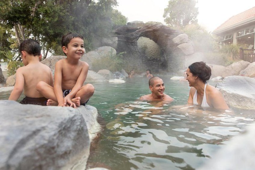 A hot spring with people sitting and standing in the water, surrounded by rocks and trees. 2