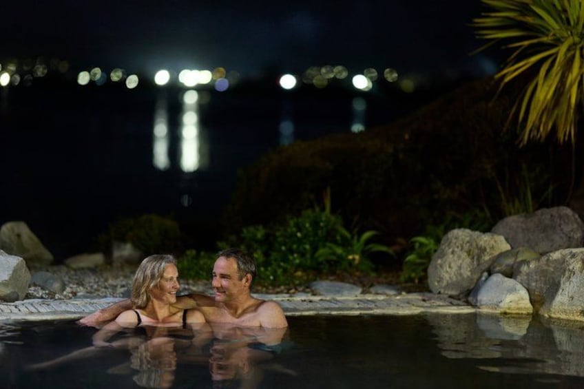 A couple in a heated outdoor pool at night with city lights in the background. 2