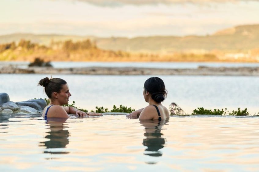 Two people in a hot tub with a lake and hills in the background. 4