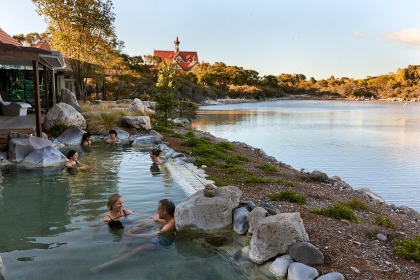 A natural hot spring with people relaxing in the water, surrounded by rocks and trees. 5