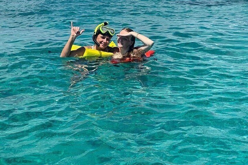 Two people floating in clear blue water, wearing life jackets and goggles. 3
