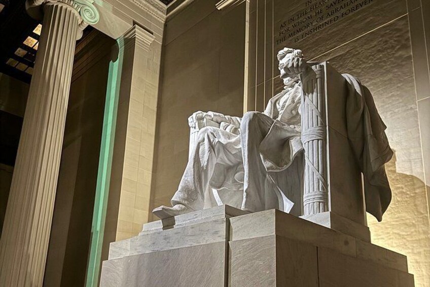 A statue of a seated figure with a draped robe, standing on a pedestal with columns, in a museum setting. 3