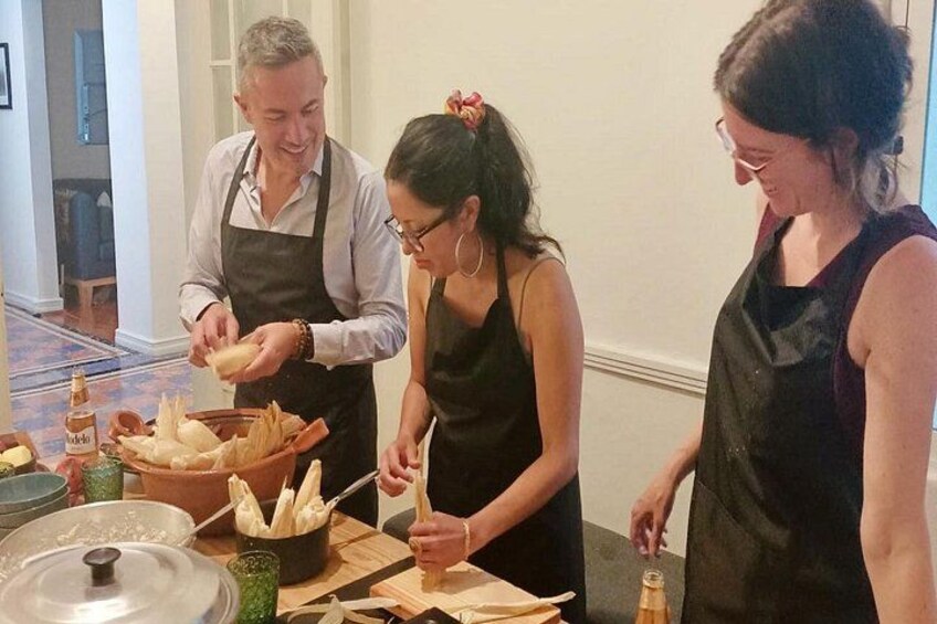 Three people preparing food, with bread and a bottle on the table. 2