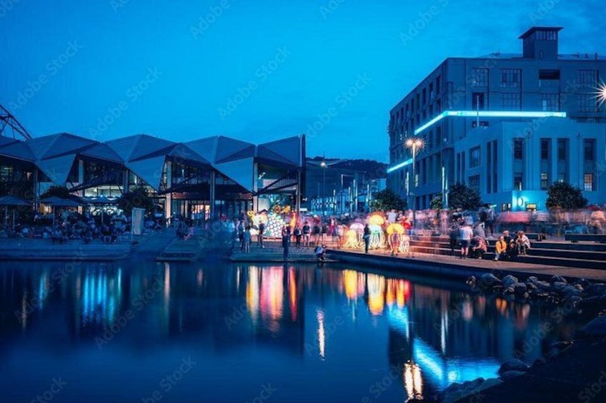 A waterfront area with modern architecture, including a building with a unique triangular roof and another with a flat facade. 1