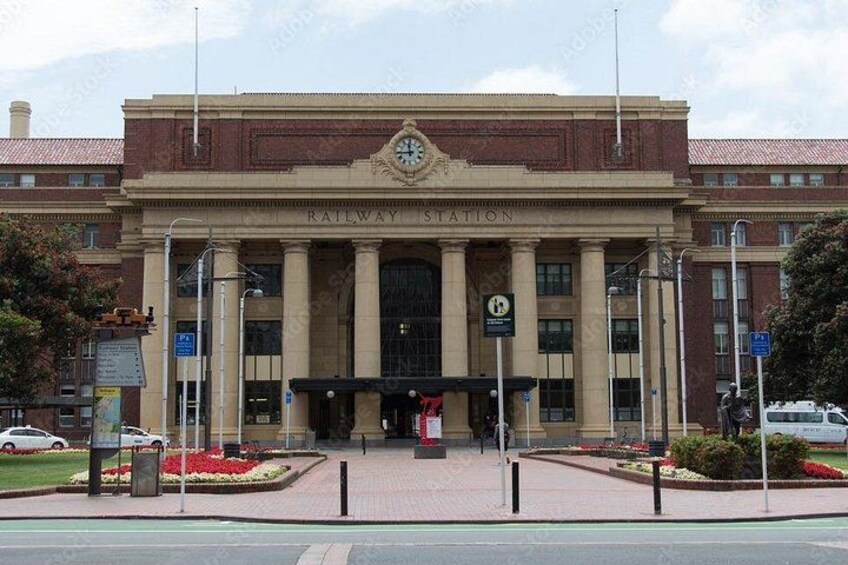 A railway station with a prominent clock tower, large columns, and a covered entrance. 5