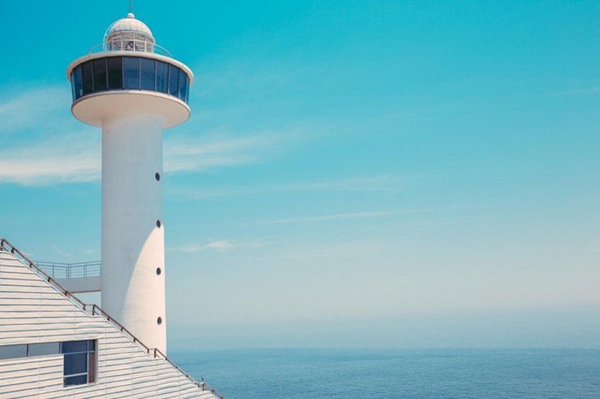 Un faro con una torre blanca y una plataforma circular de observación, que domina un mar en calma. 5