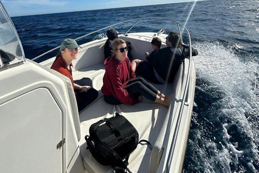 A boat with four people on board, one person steering, and a black bag on the floor. 3