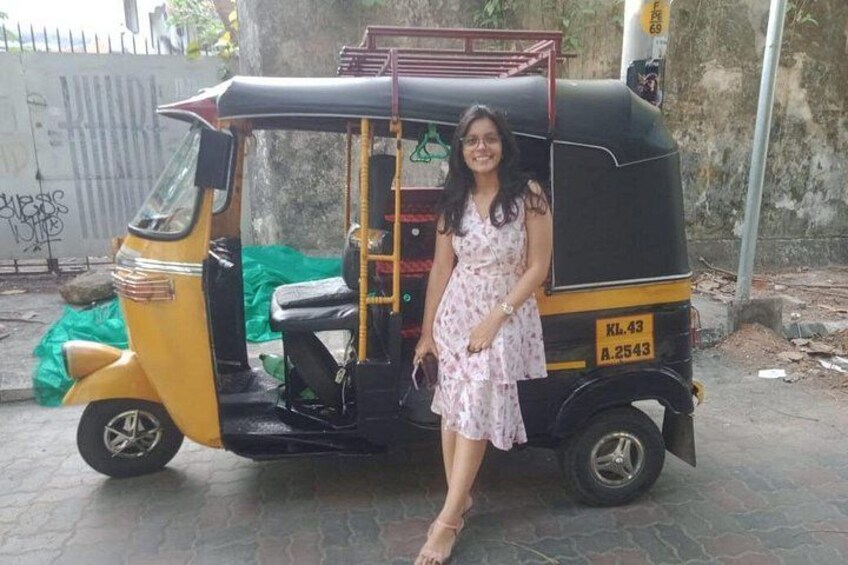 A woman in a floral dress standing next to a yellow auto-rickshaw with visible license plate KL 43 A 2543. 5