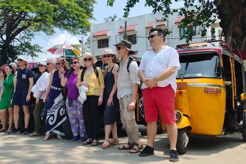 A group of people standing in line, a yellow auto-rickshaw, and buildings in the background. 2