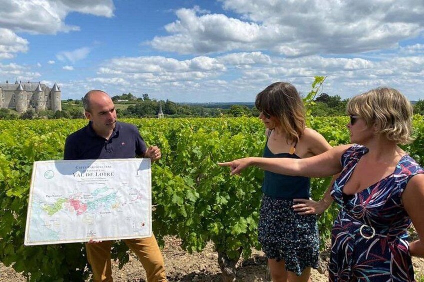 Drei Personen in einem Weinberg, mit einer Karte und einer Burg im Hintergrund. 2