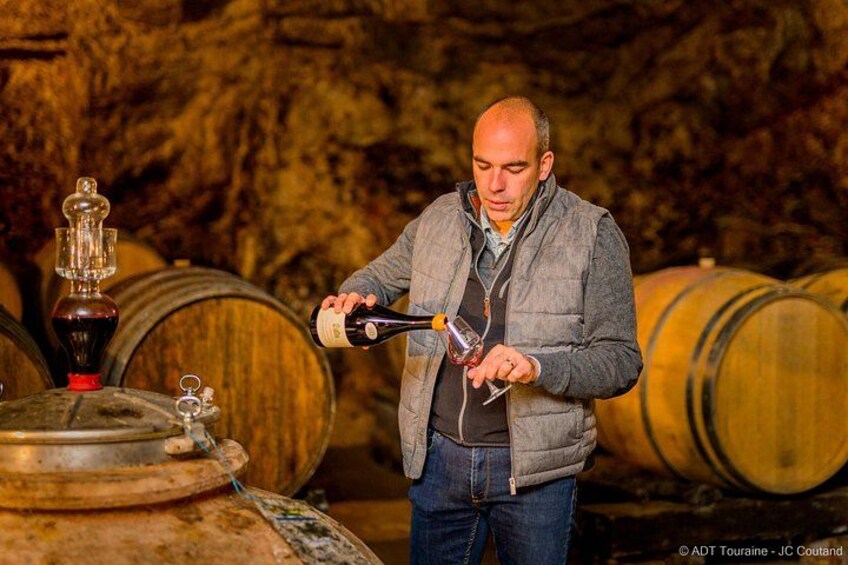 Eine Person schwenkt Wein aus einer Flasche in ein Glas. Im Hintergrund sind Holzbärge zu sehen. 3